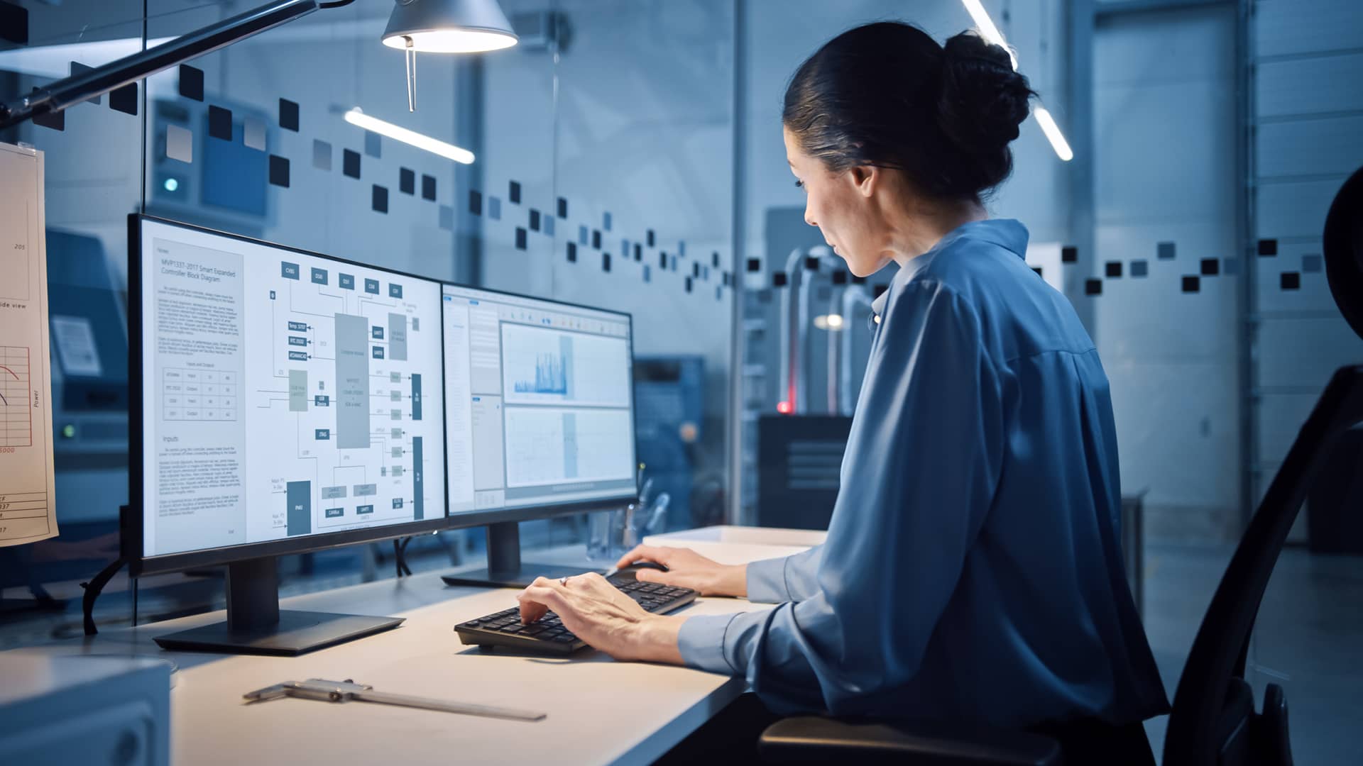 Portrait of a female Industrial Engineer working on computer, using industrial electronics design software containing intellectual property. In the background is a high tech facility with CNC machinery.