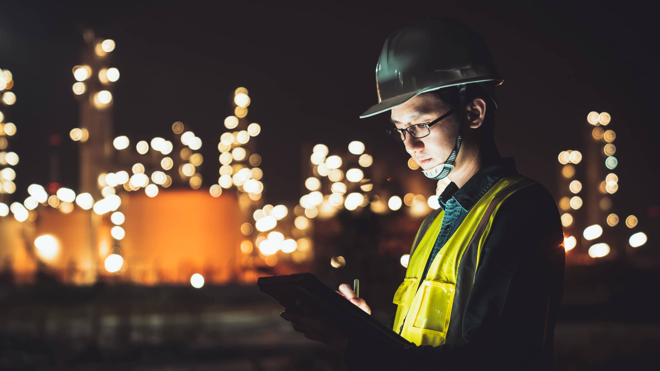 Engineer using a digital tablet outside a petrochemical facility during the night.
