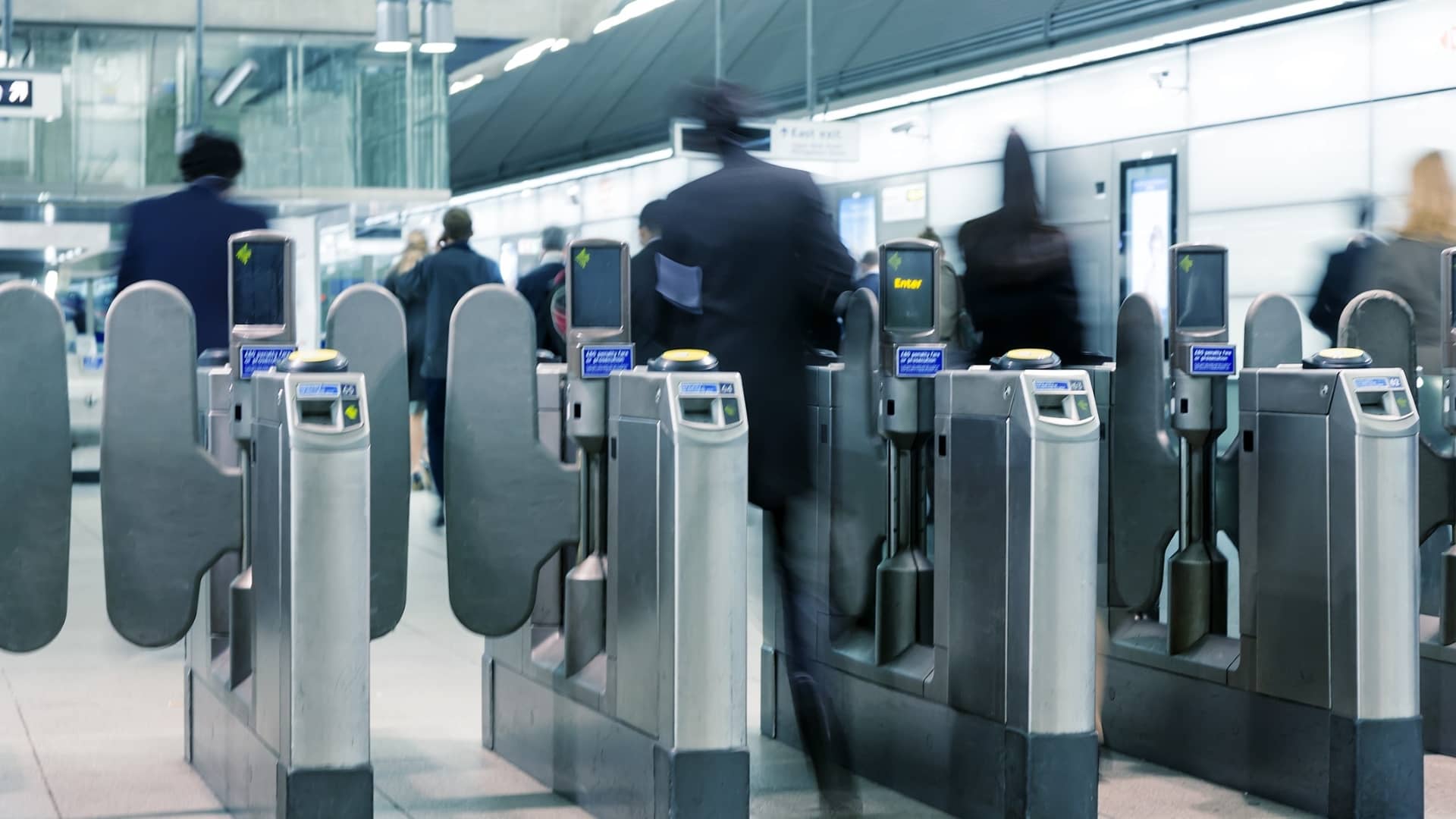 Motion blurred unrecognizable businesspeople walking into a subway station in London through the ticket gates.