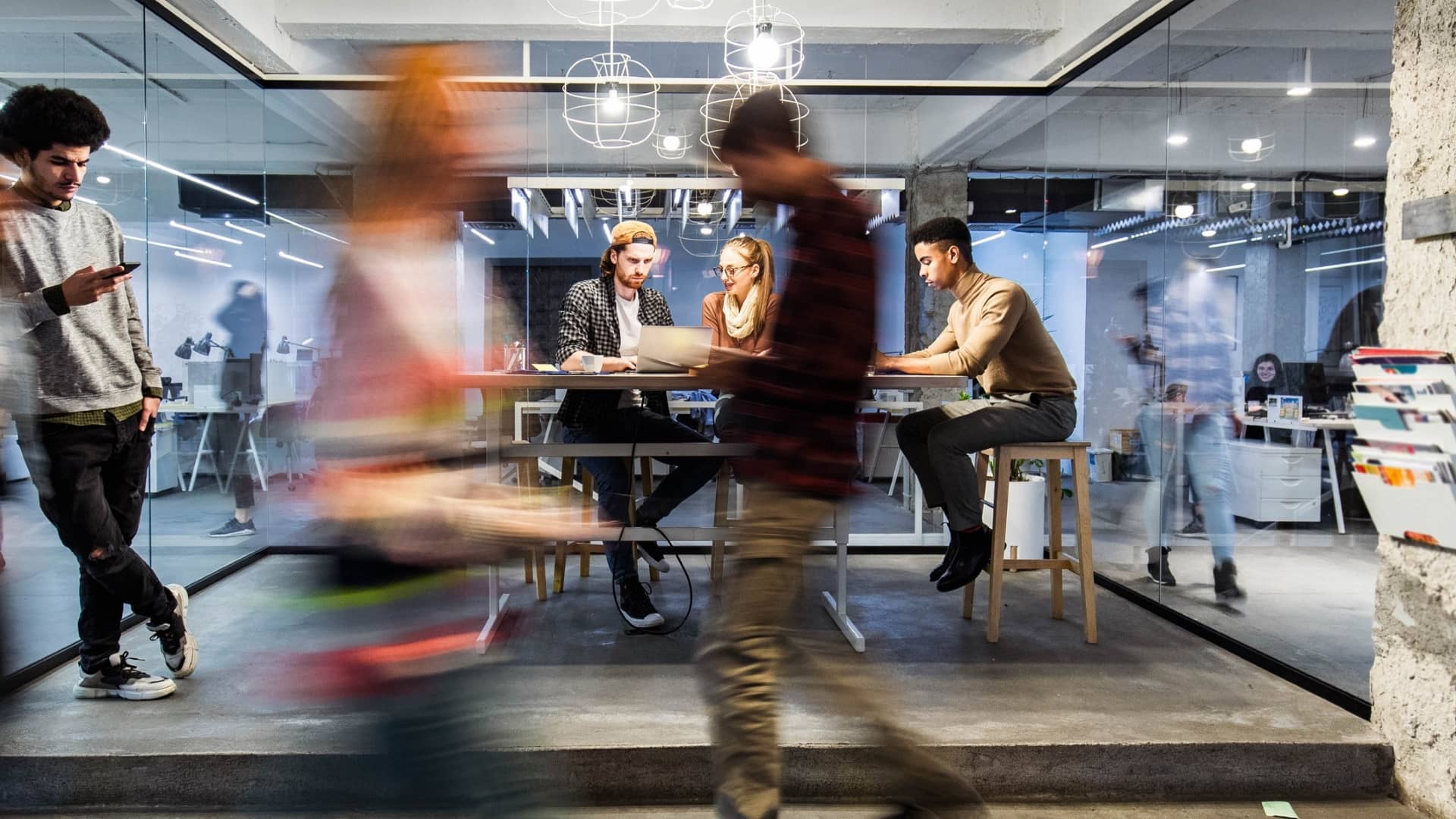 Group of young freelancers working on wireless technology at casual office. Some people are in blurred motion.