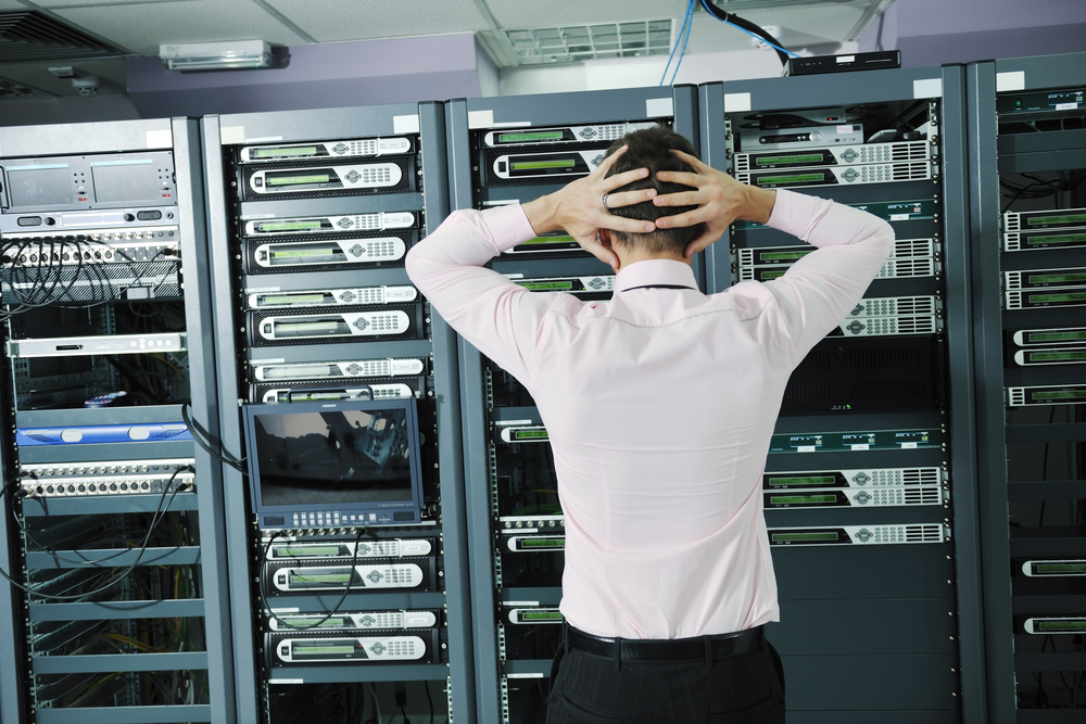 A businessman looking stressed in front of a rack of computer servers to signify the role of human error in data security.